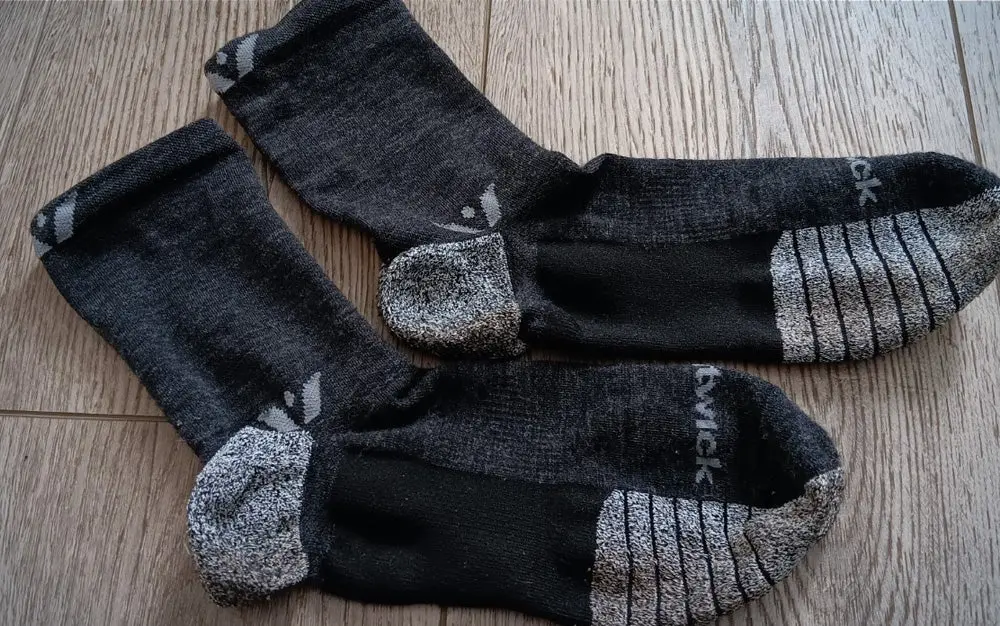 A pair of black and grey Swiftwick trail socks on a hardwood floor.