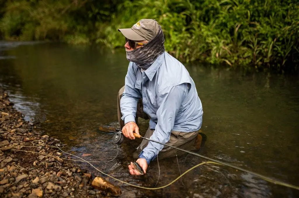 Angler kneeling by a river with a mountain mullet.