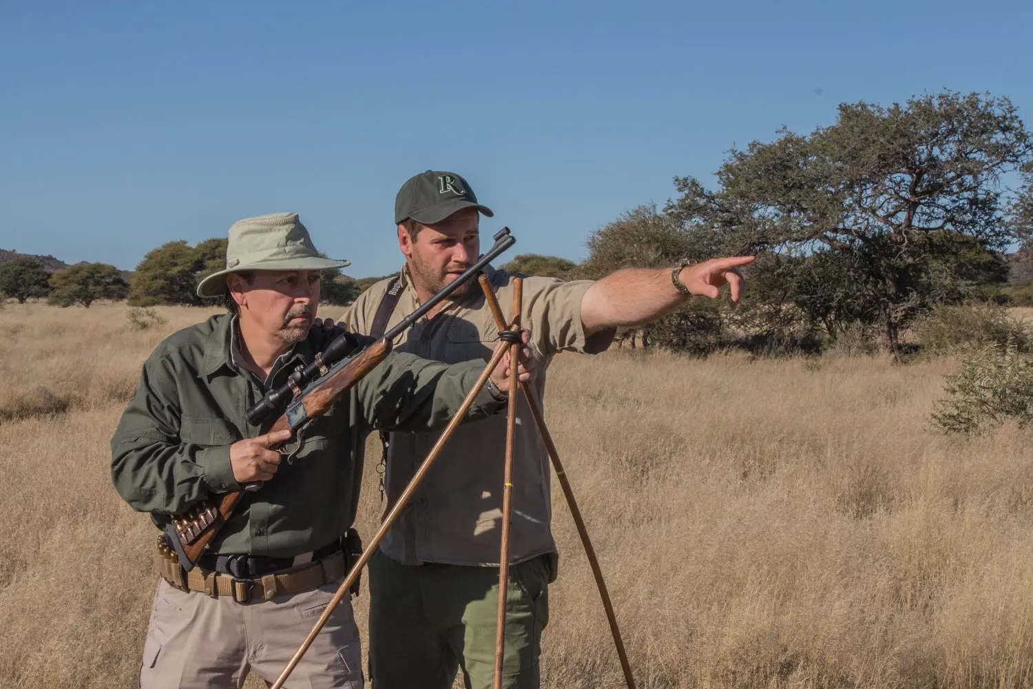 A hunter prepares to fire off shooting stick as his guide points to the target