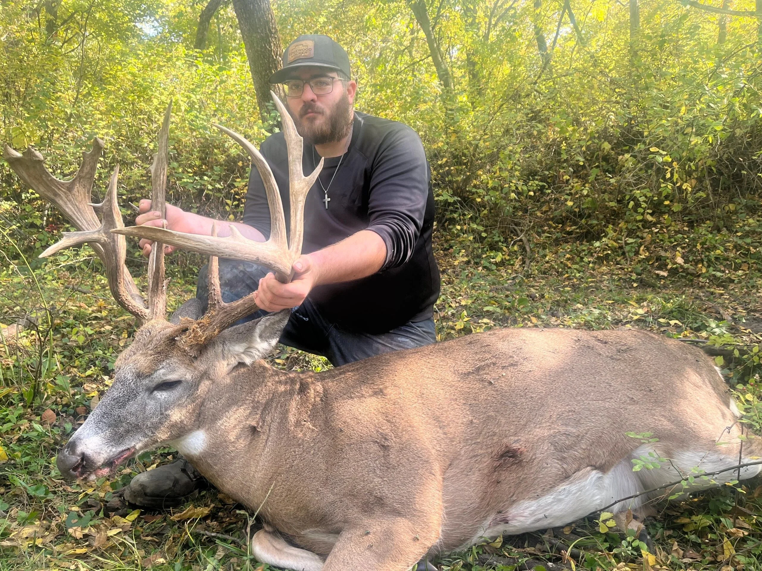 hunter sitting next to dead whitetail buck.