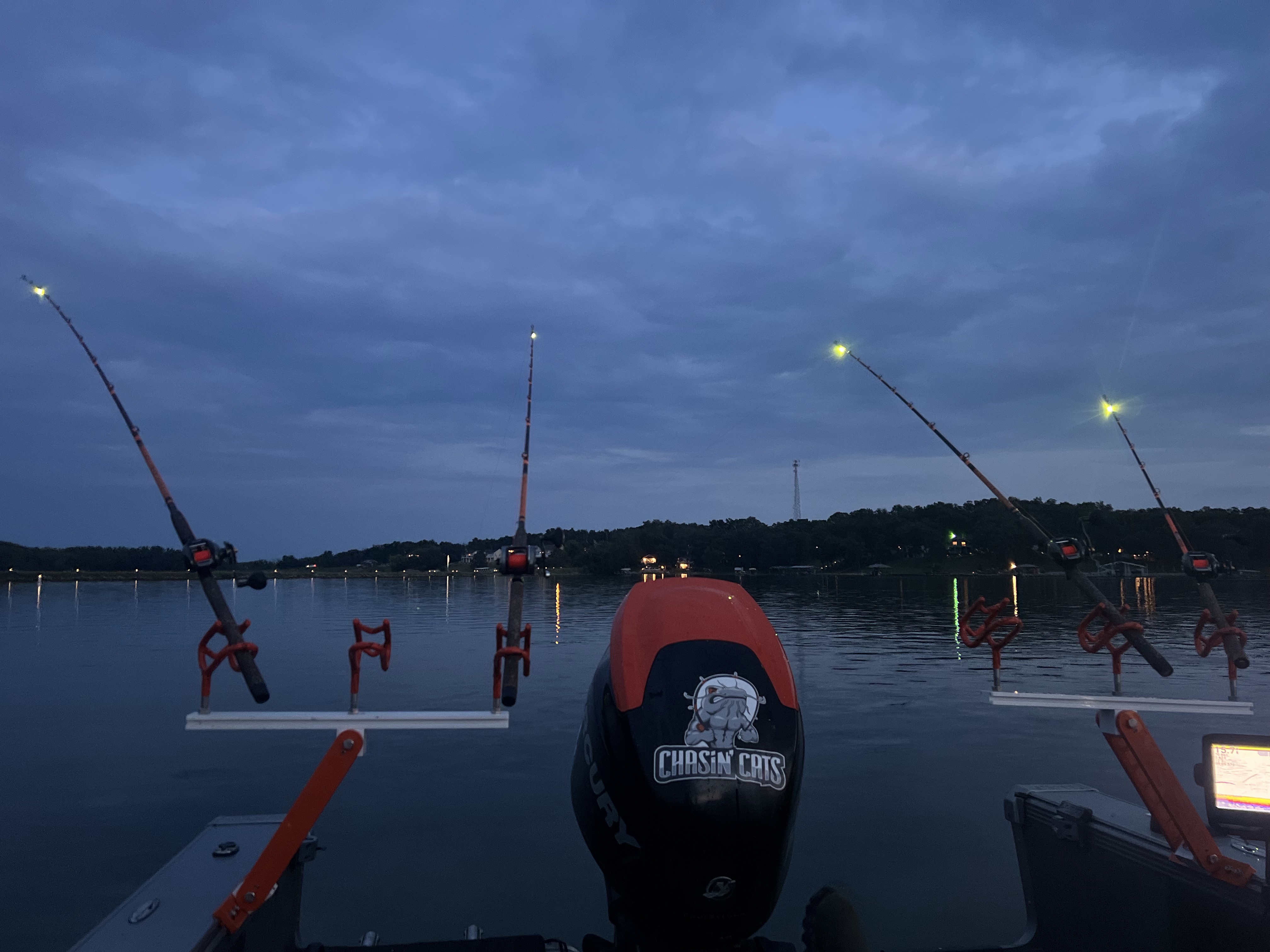 Four fishing rods rig in rod holders on the stern of a boat with lights attached.