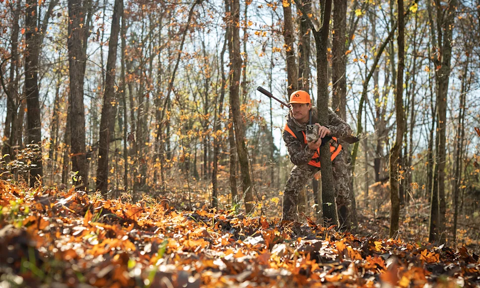 A hunter sets up a trail camera in the woods.