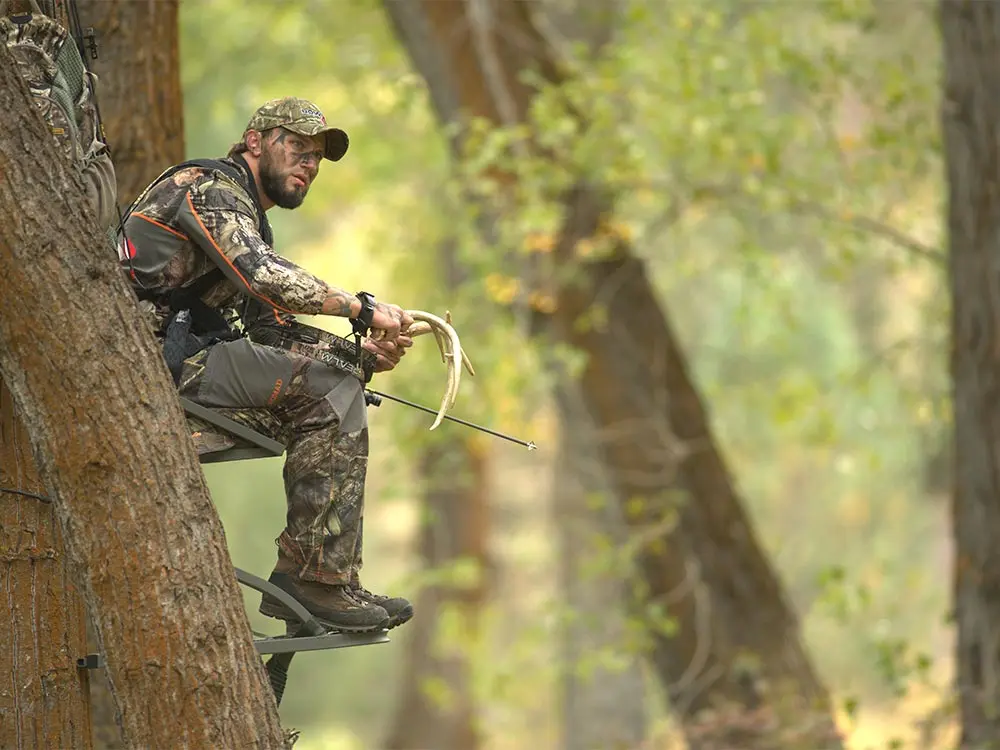 deer hunter rattling antlers in a tree stand