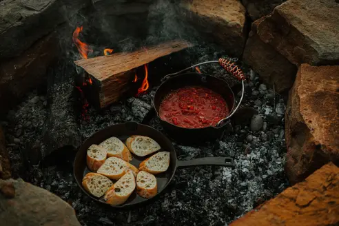 Two dutch ovens laying in coals of campfire