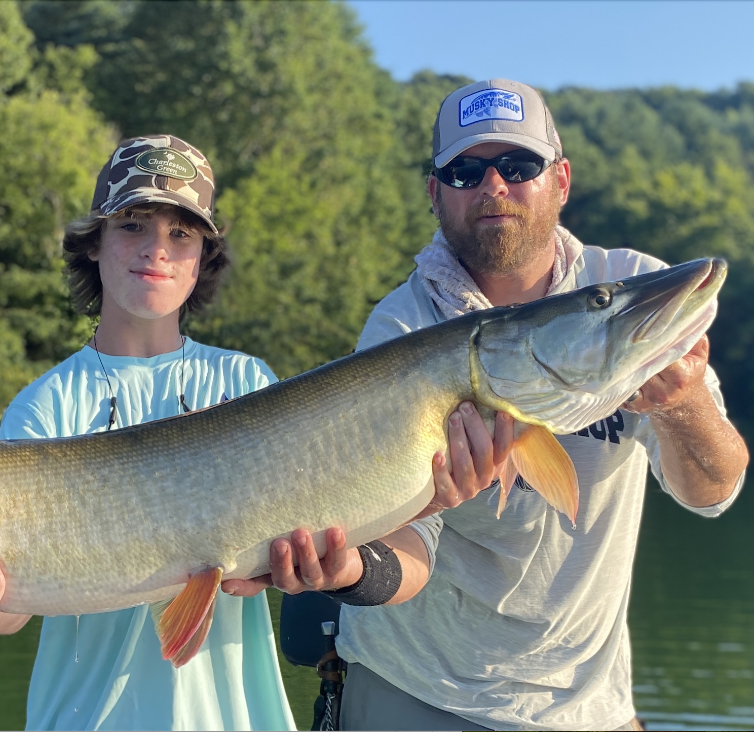 A pair of angler hold up a big muskie caught from a lake. 