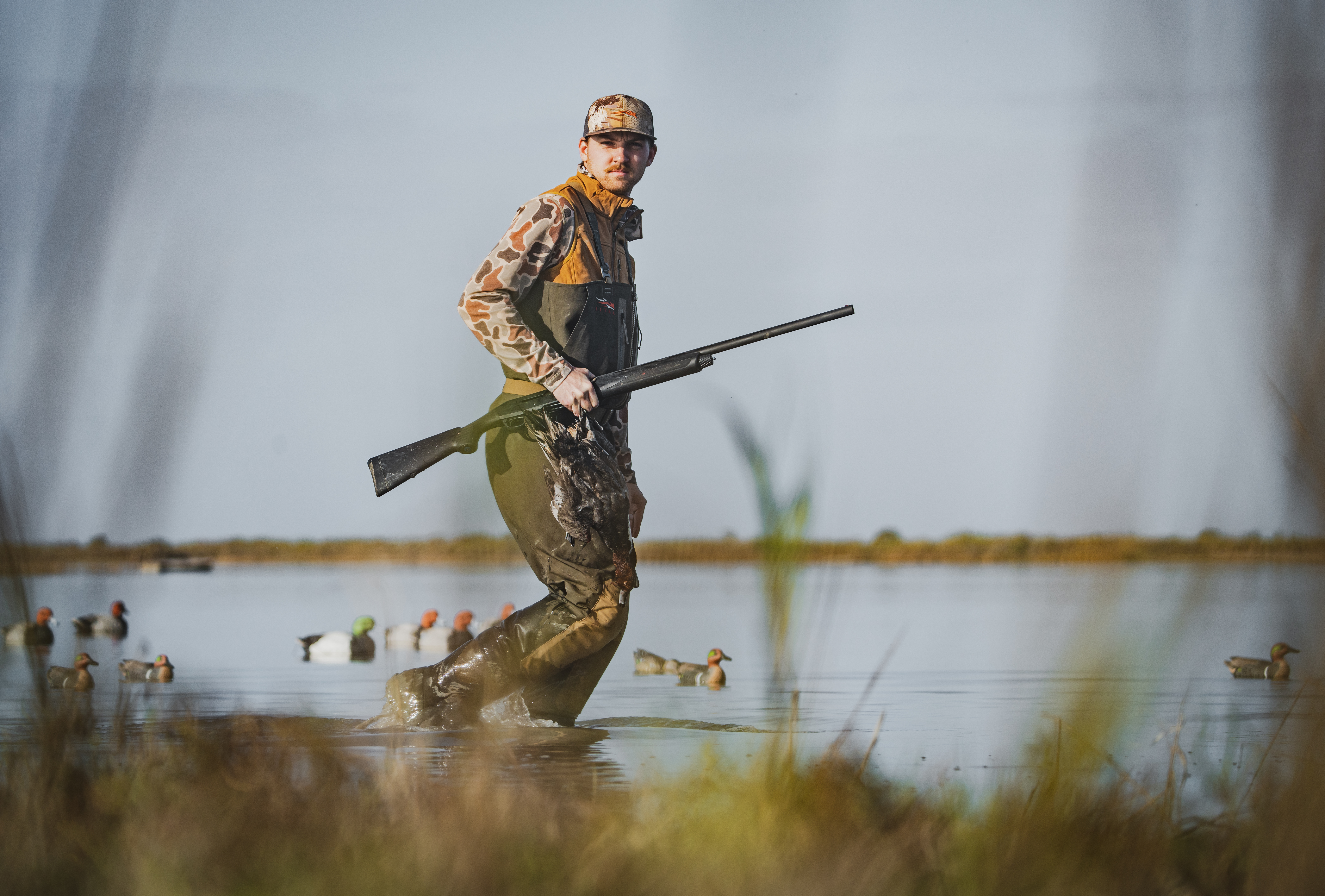 Hunter walking through water with shotgun and duck