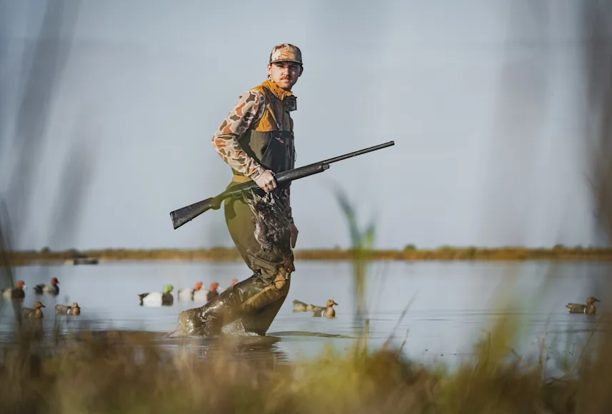 Hunter walking through water with shotgun and duck