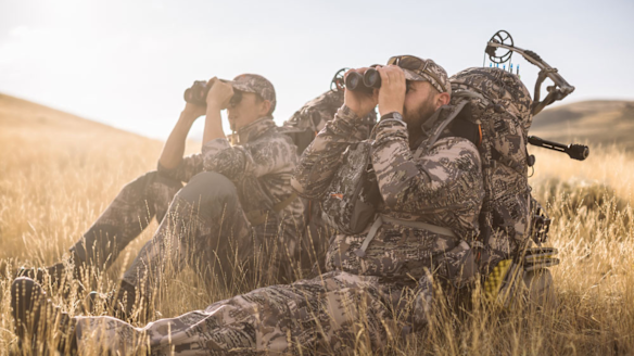 Two bowhunters looking through binoculars wearing Sitka Gear