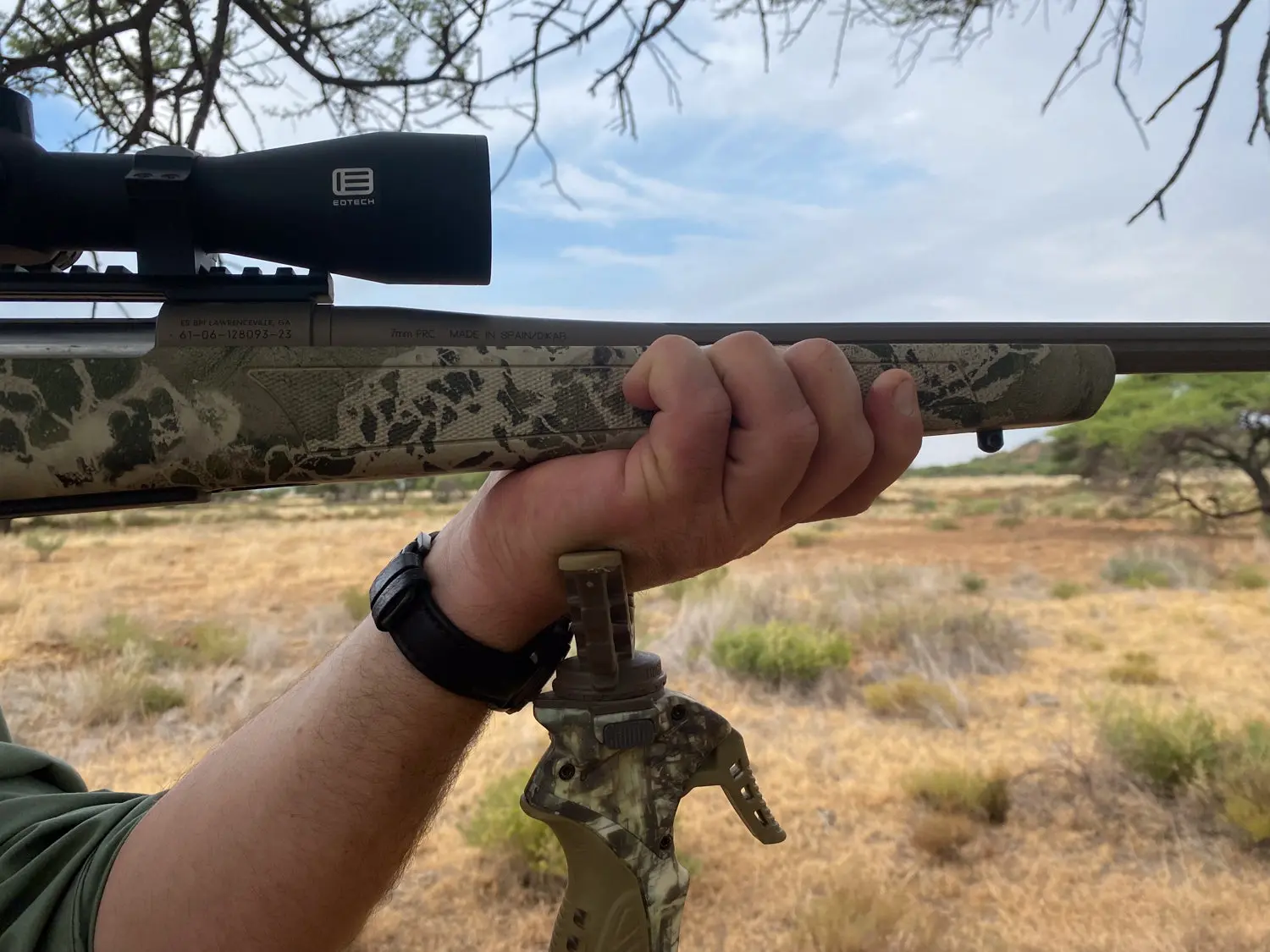 A shooter holds the forend of rifle while resting his hand on the top of a shooting stick.