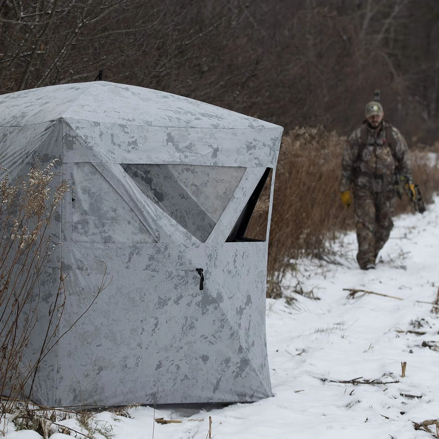 A hunter walks toward a snow-camo hunting blind. 