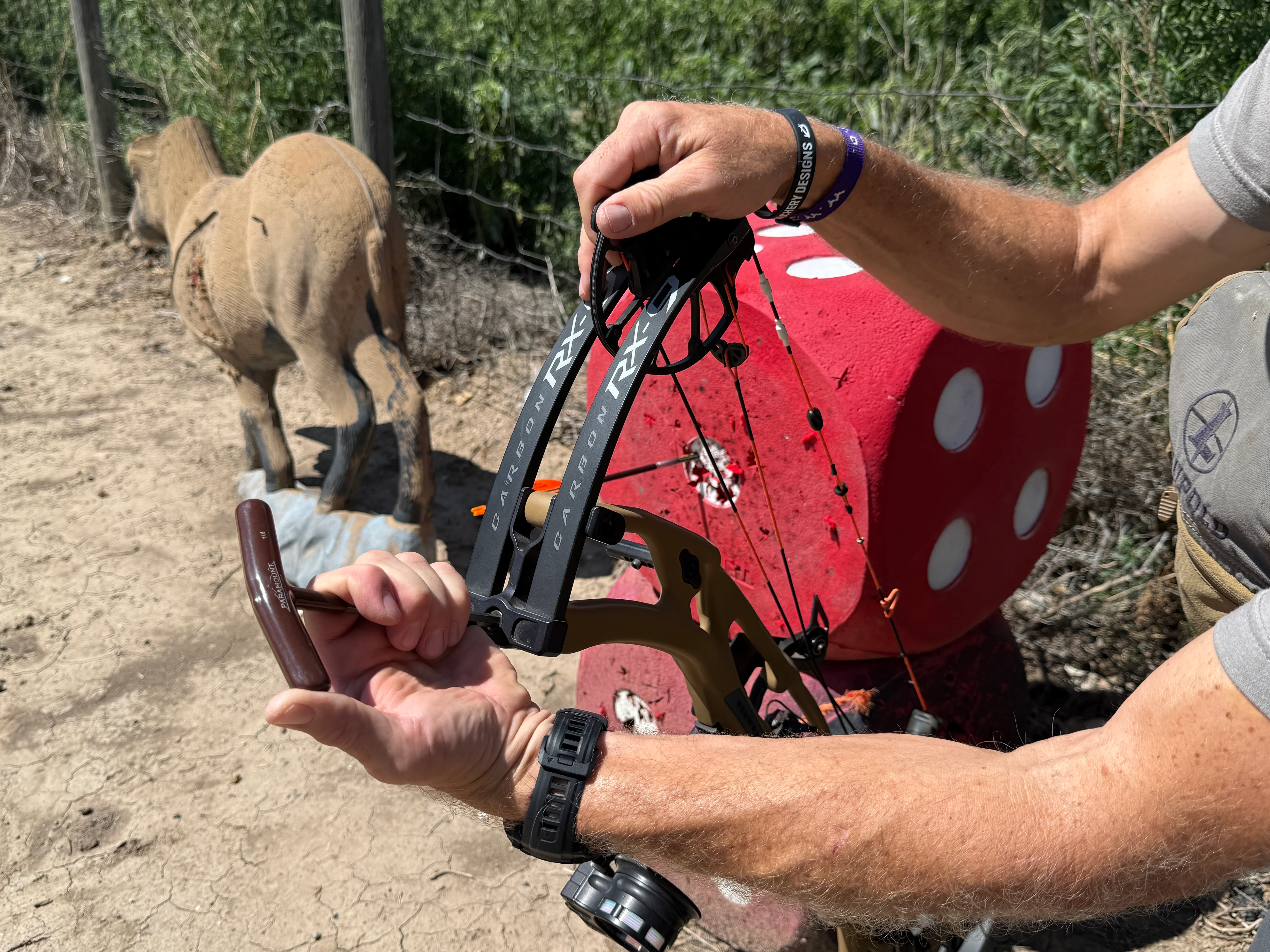An archer adjusts the draw weight on a compound bow while standing on a bow range. 