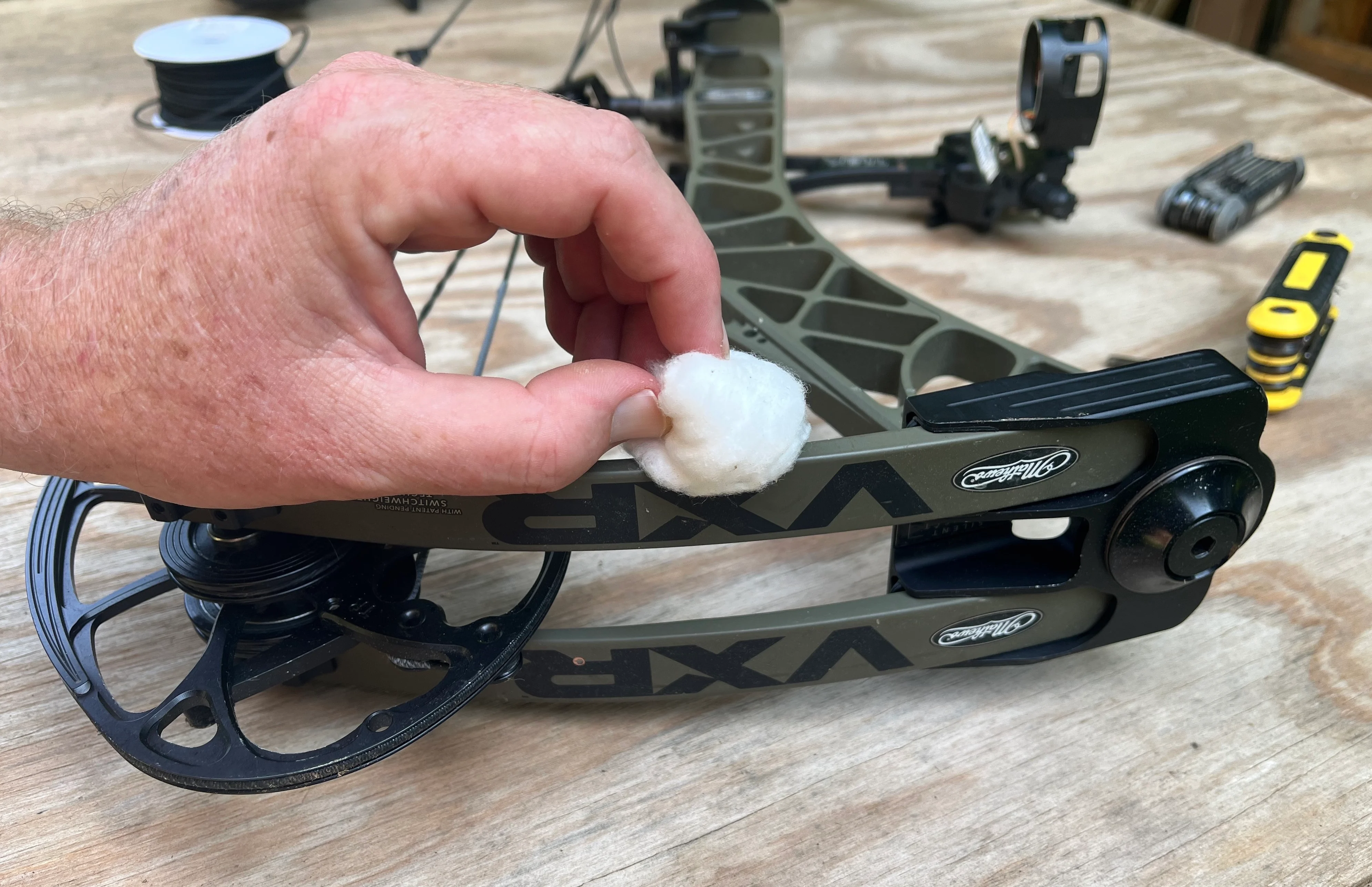 A man's hand run a cotton ball along the limb of a compound bow. 