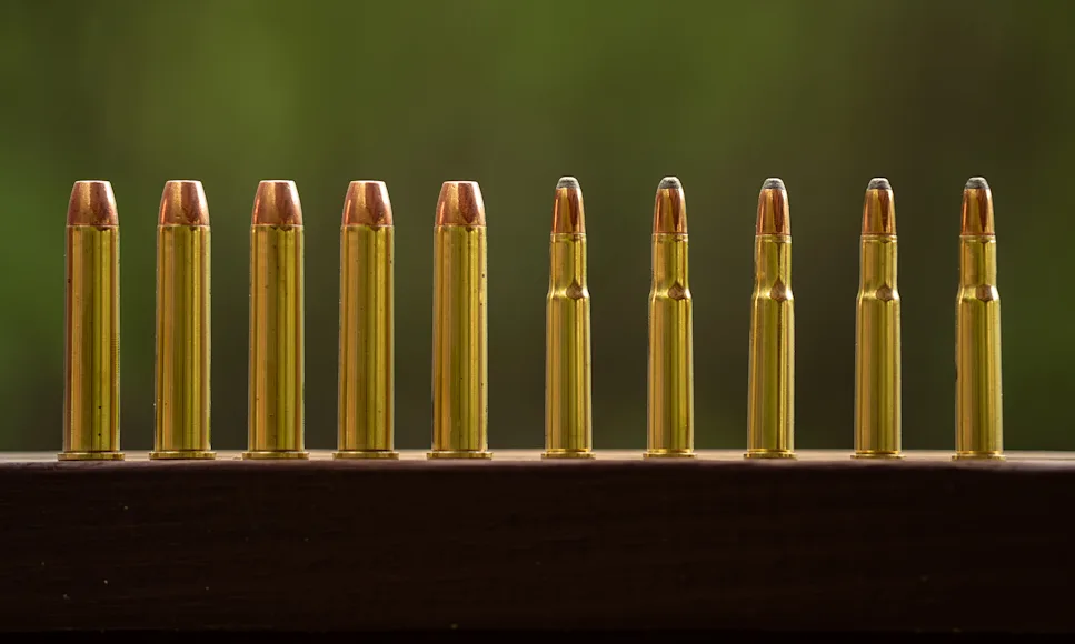 A row of 45-70 vs 30-30 cartridges, lined up on a railing.