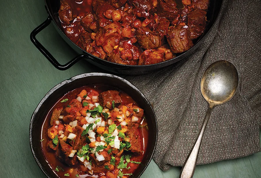 A bowl of venison posole next to a pot of the venison stew sitting on a table.