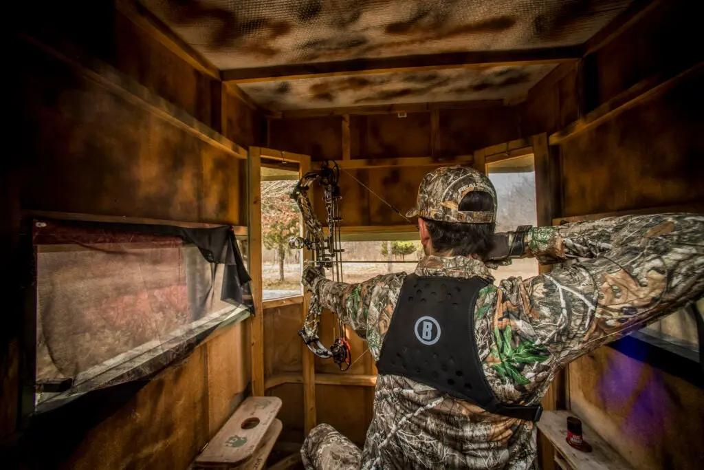 Bowhunter shoots a compound bow in a blind