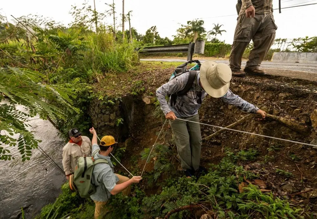 Anglers climbing up a hillside away from a river.