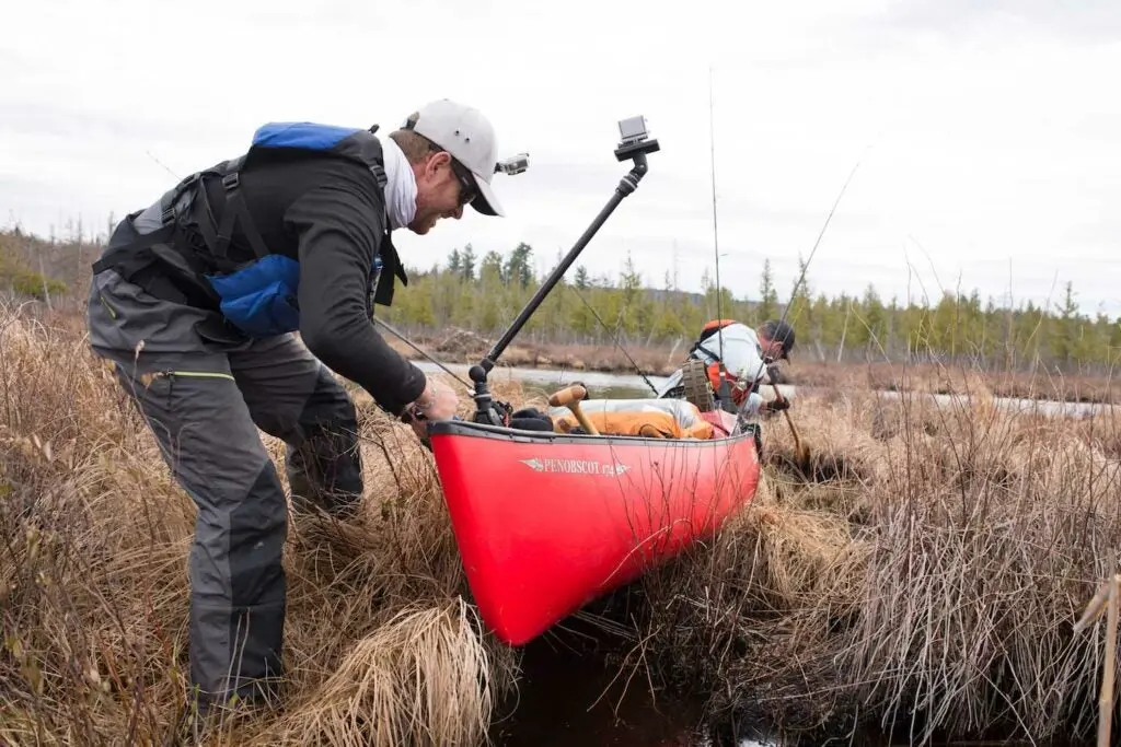 A paddler drags a canoe through grass to the water in Upstate New York.