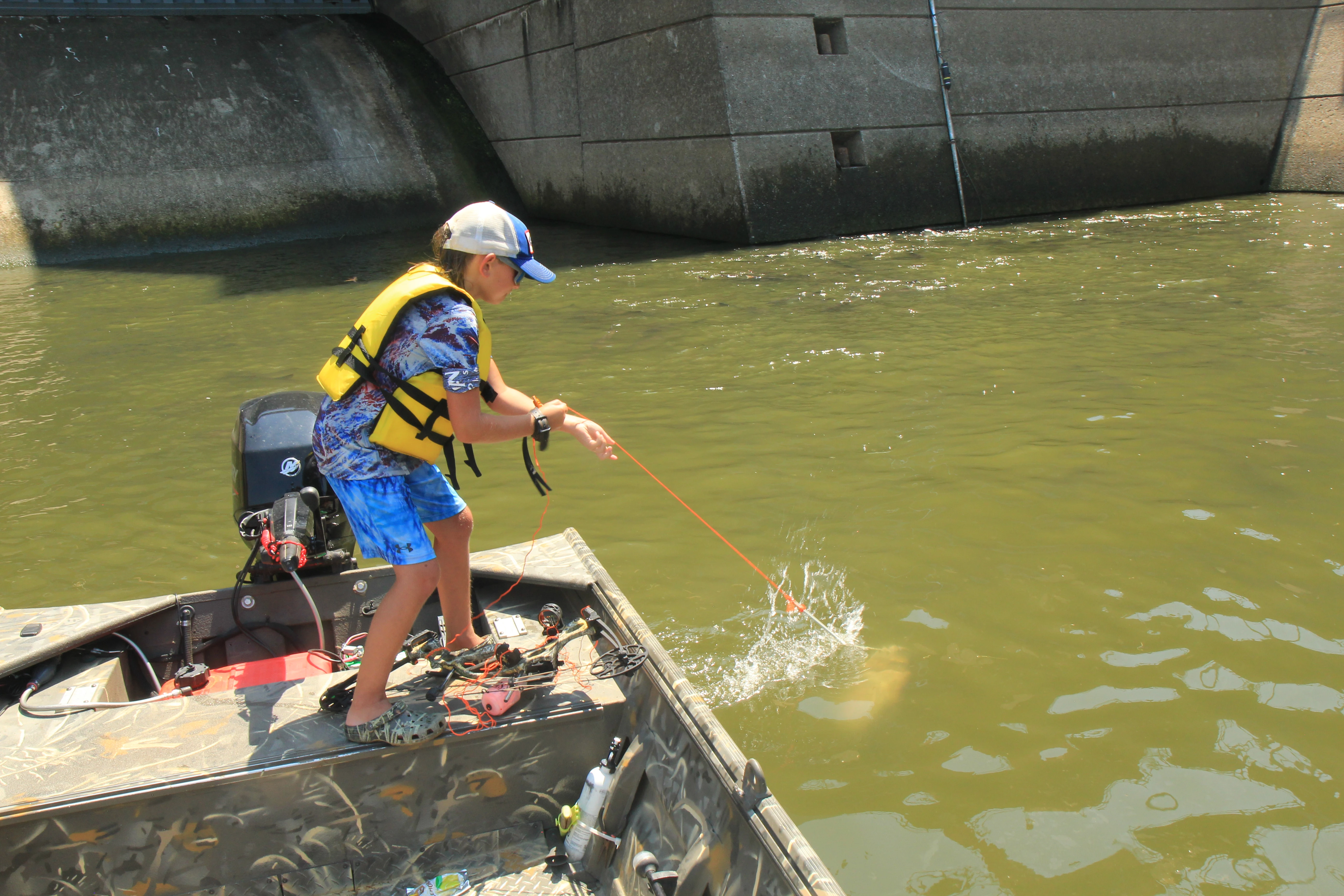 A kid in a life jacket pulls in a carp with his hands