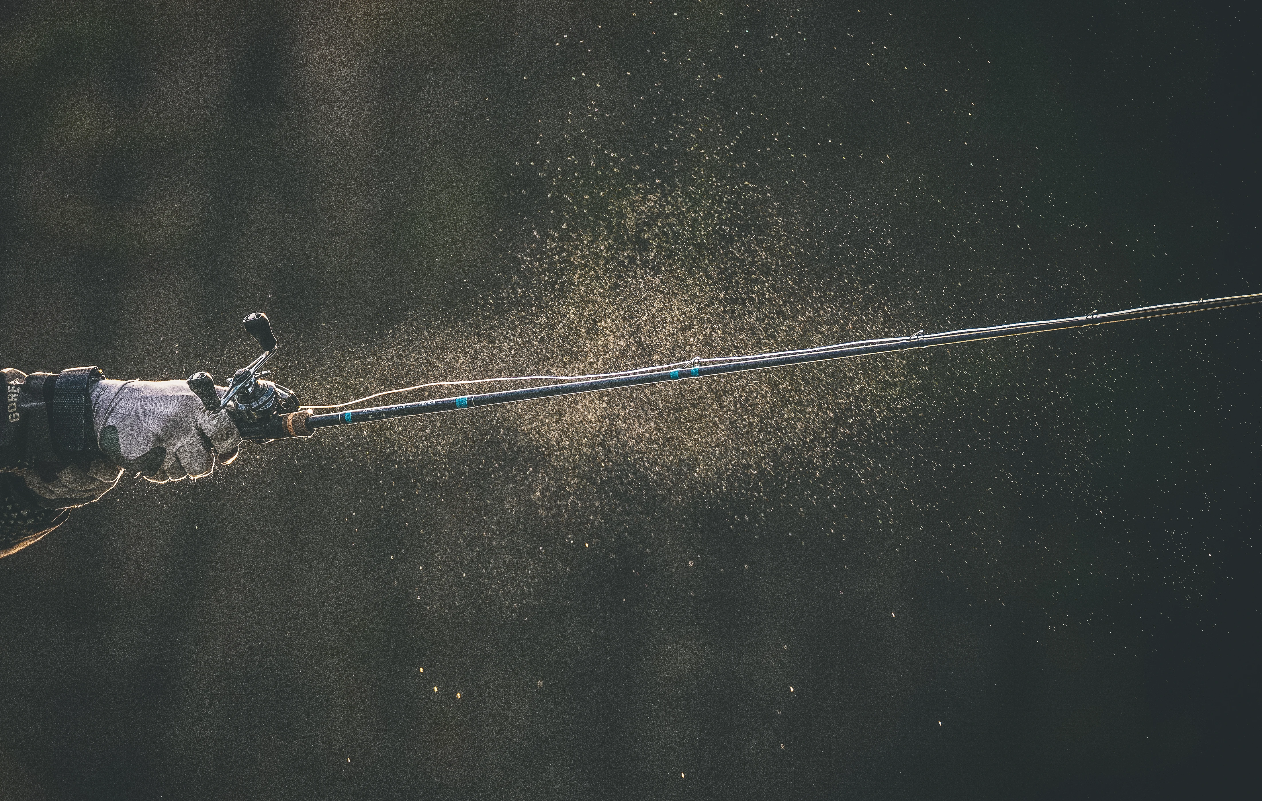 Photo of a rod and reel while an angler cast and water comes off the line