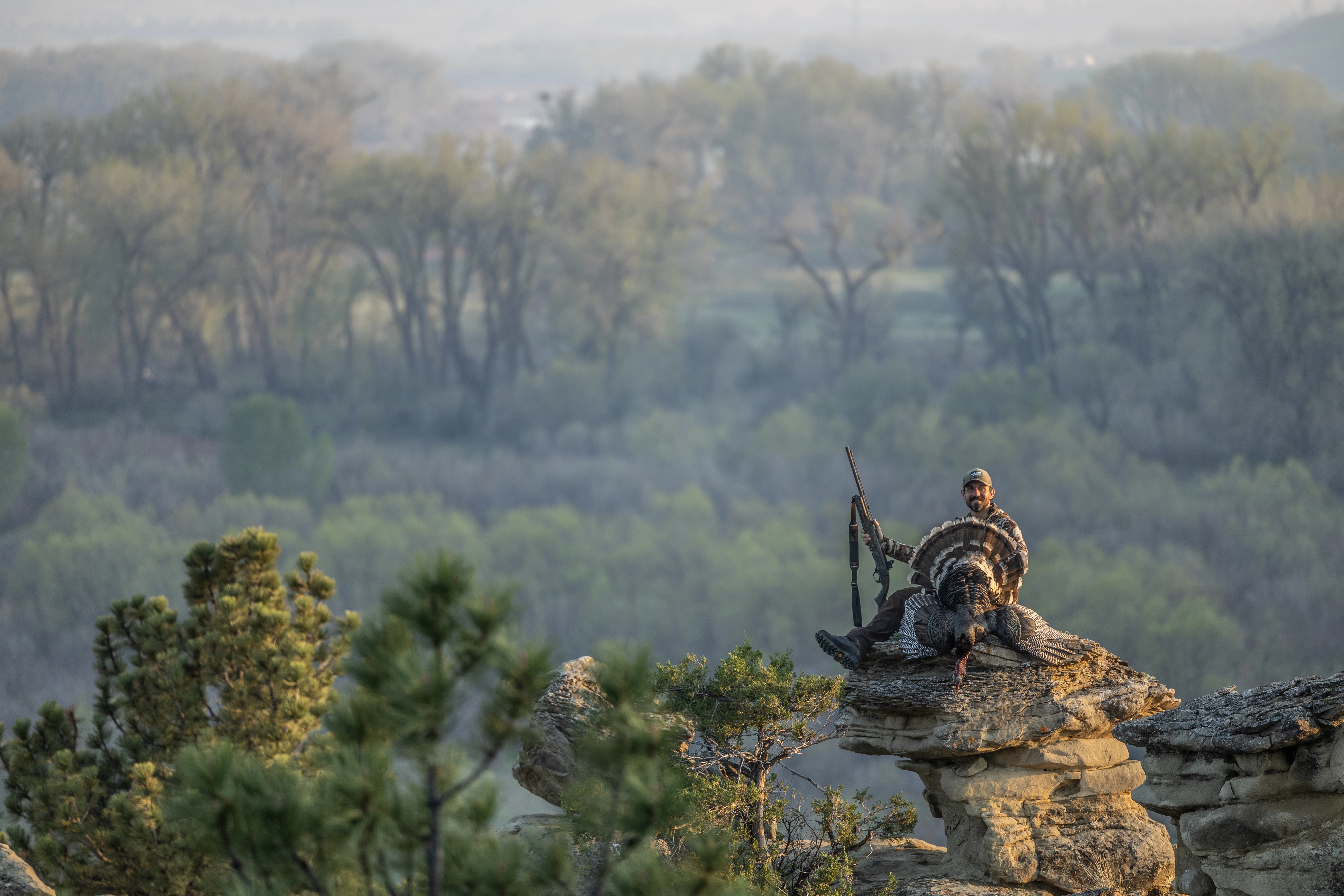 A hunter sits on a mesa with a turkey