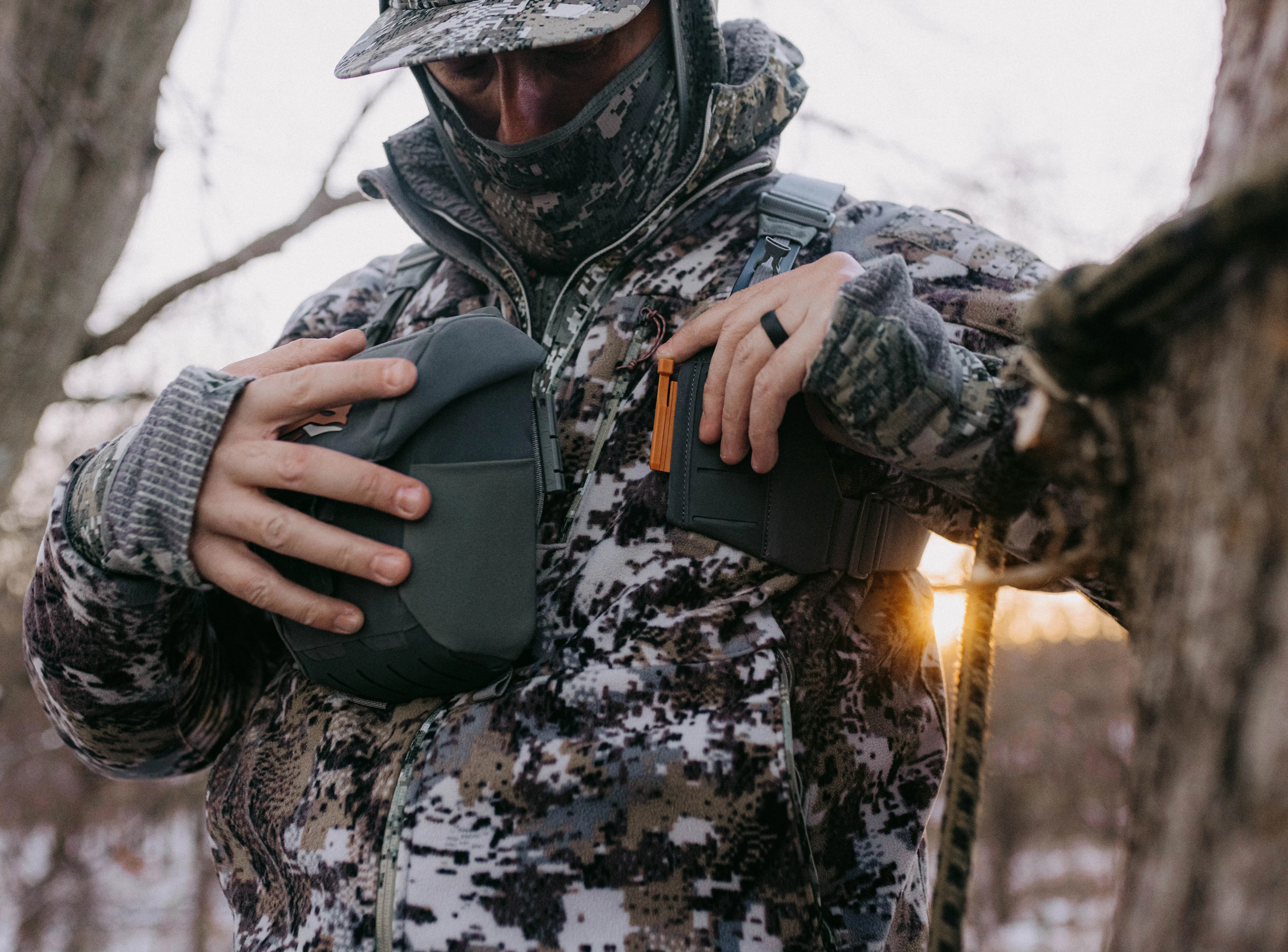 A treestand hunter puts on Sitka's Flash Optics bino harness. 