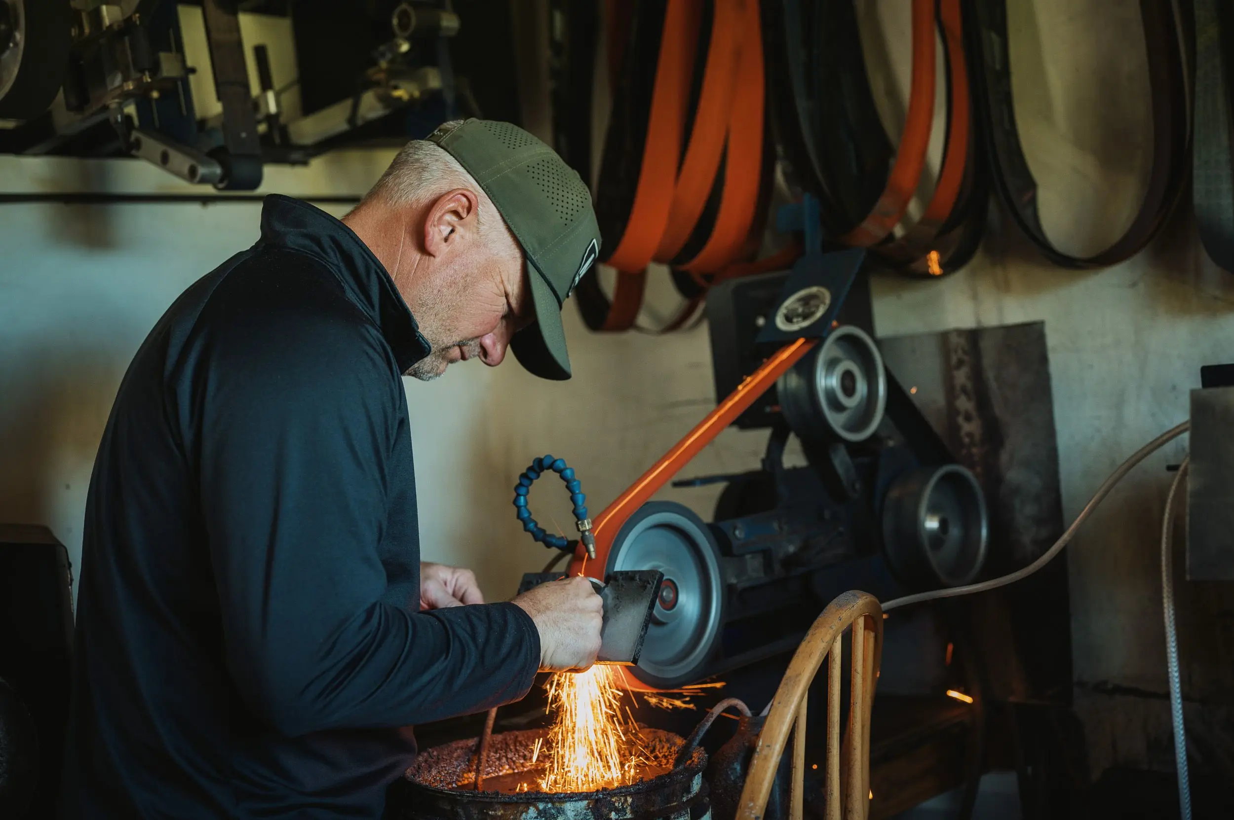 A knife maker sharpens a knife on a belt grinder. 