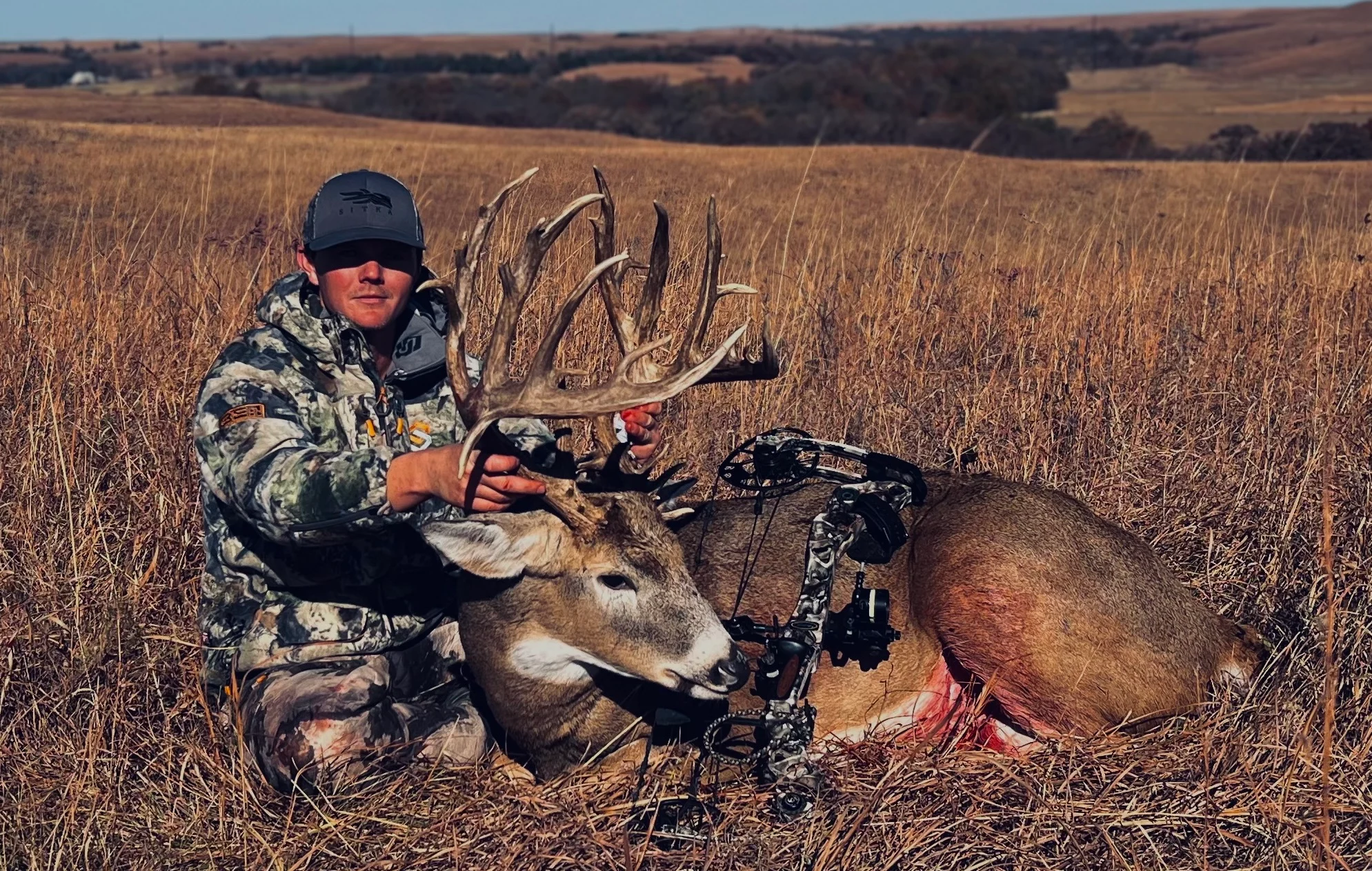 Kansas hunter poses in a field with a huge whitetail buck taken with a bow. 