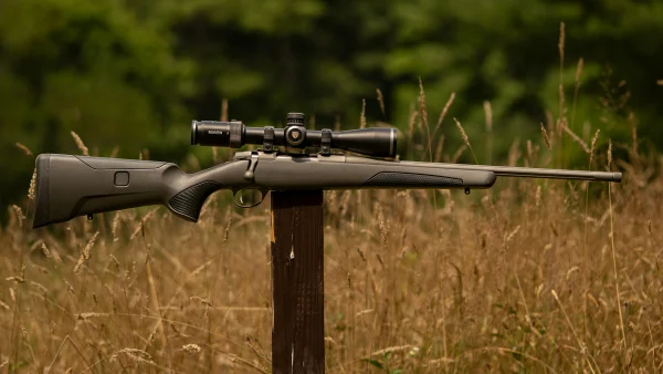 Sako 90S Adventure Rifle on a post in a field with grass and trees in background.