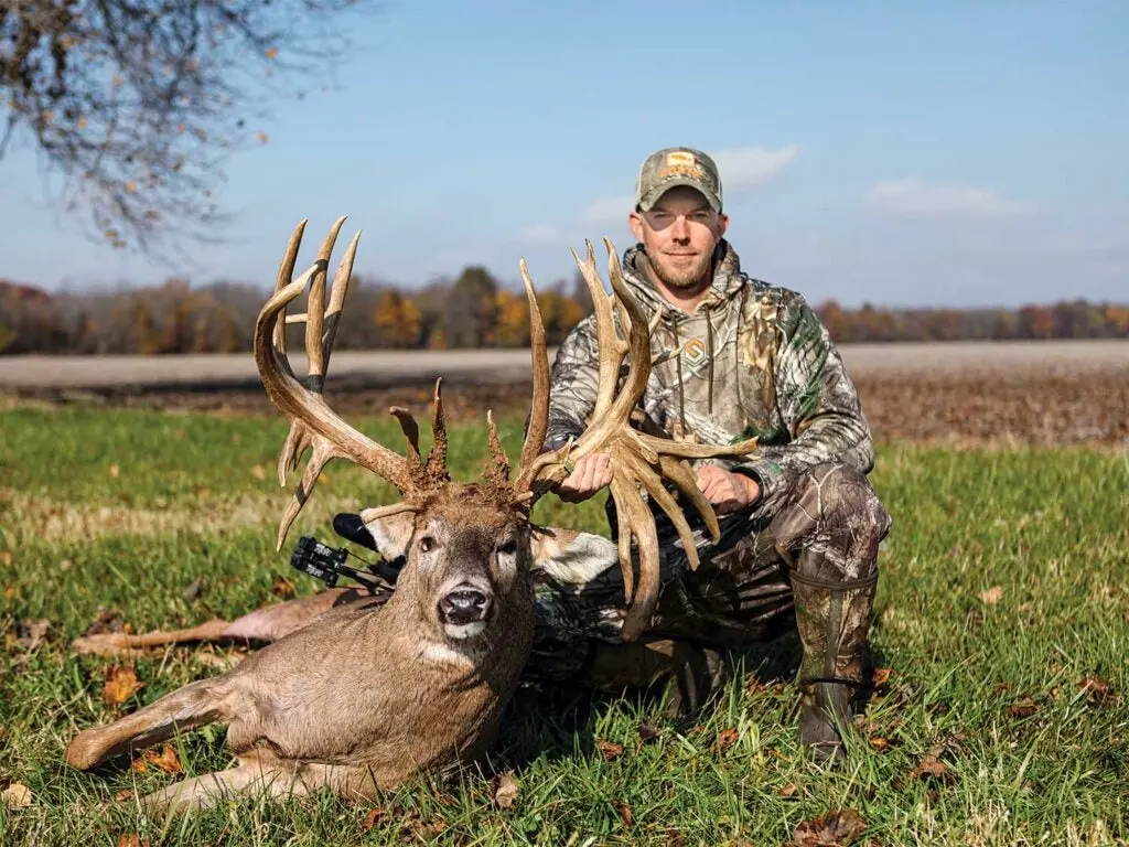 Luke Brewster kneeling beside a world-record buck.