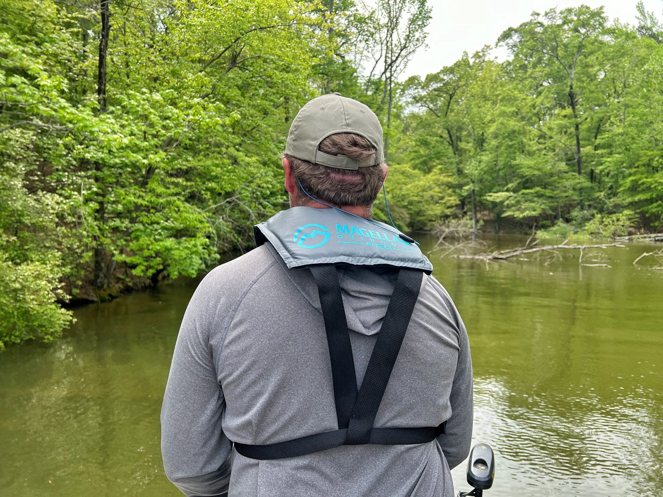 An angler in a boat facing away and wearing PDF, with a lake cove in the background.