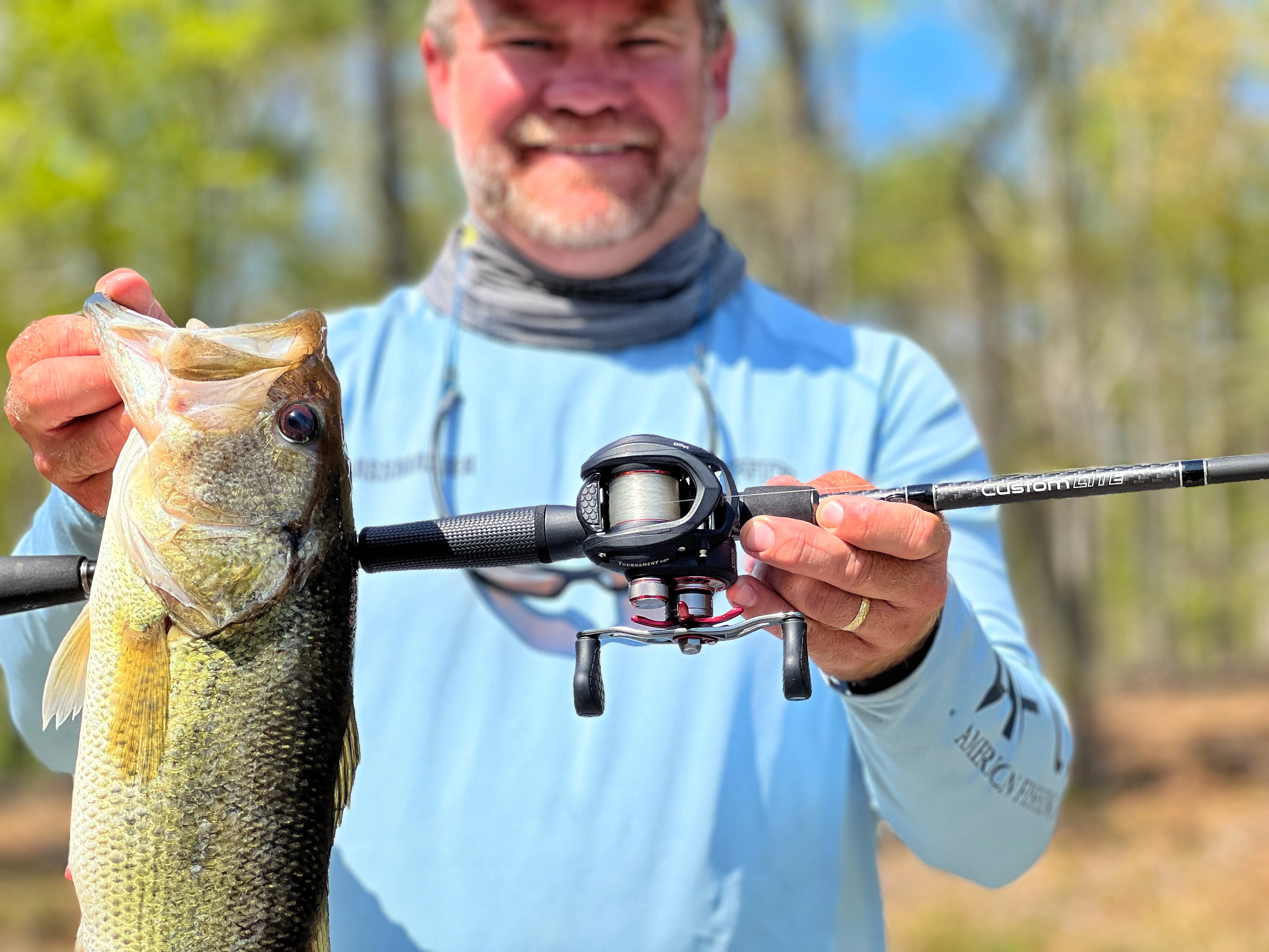 Angler holding up largemouth bass along with Lew's Rod