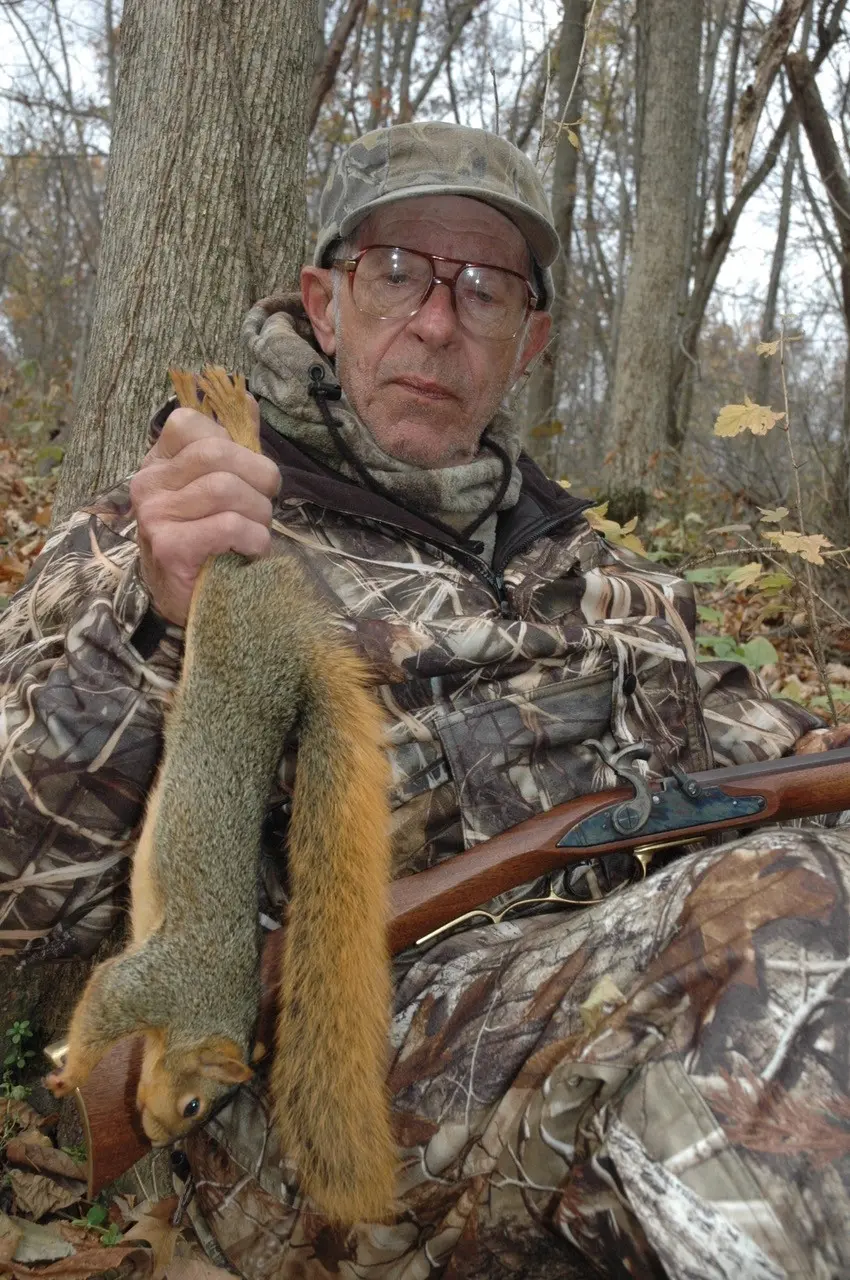 Hunter holds up a squirrel with muzzleloader in his other hand.