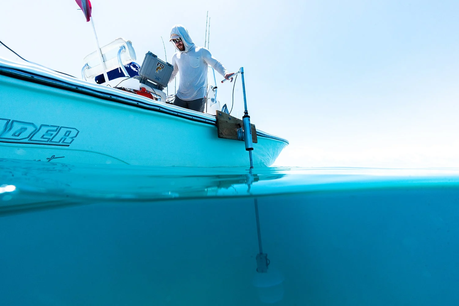 researcher on boat has hand on top of hydrophone, which stretches down into water below boat