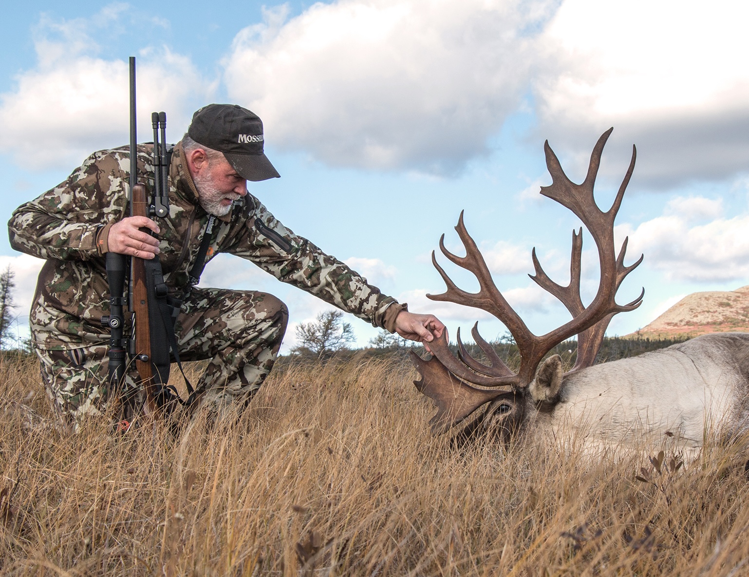 Photo of a hunter admiring a woodland caribou he took with a rifle. 