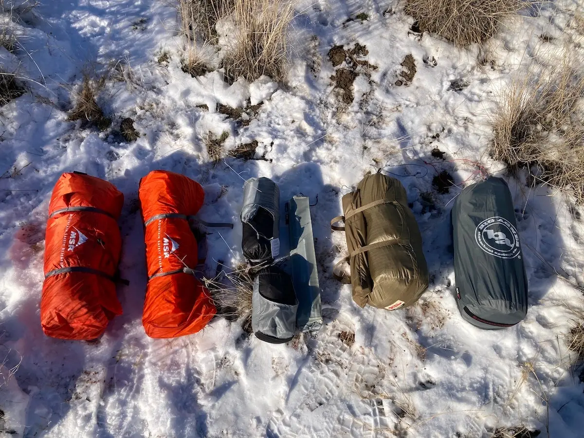 4-season tents rolled up and lined up on snow during testing