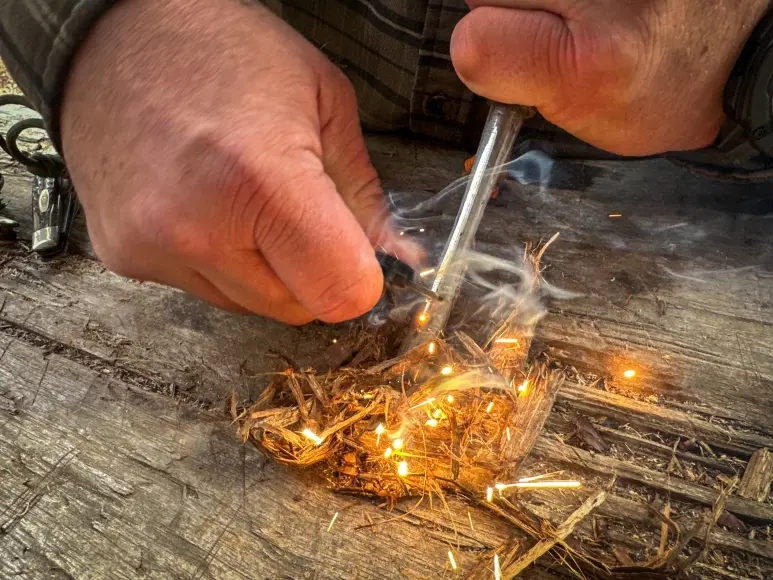 Using a ferro rod to spark fire onto a bundle of tinder