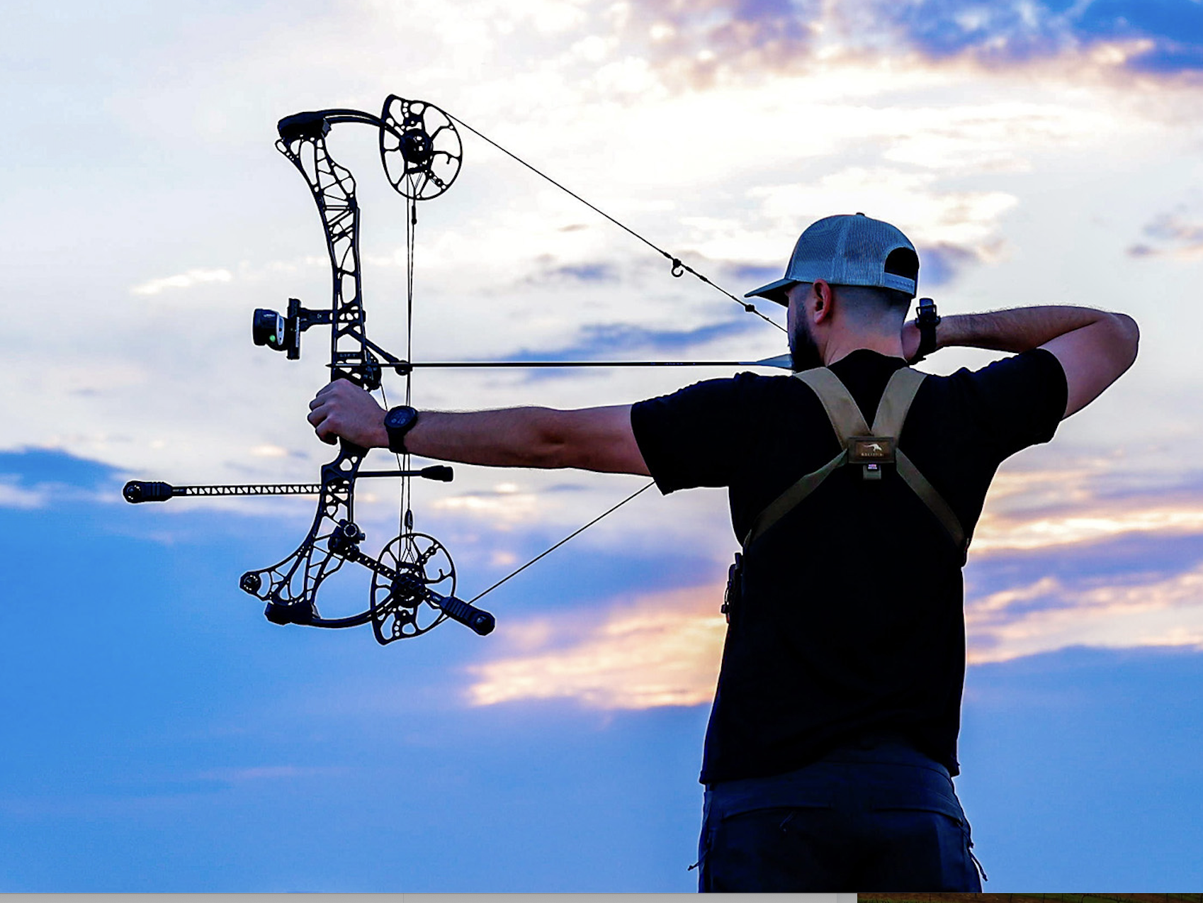 A hunter shoots a bow with sky in the background. 