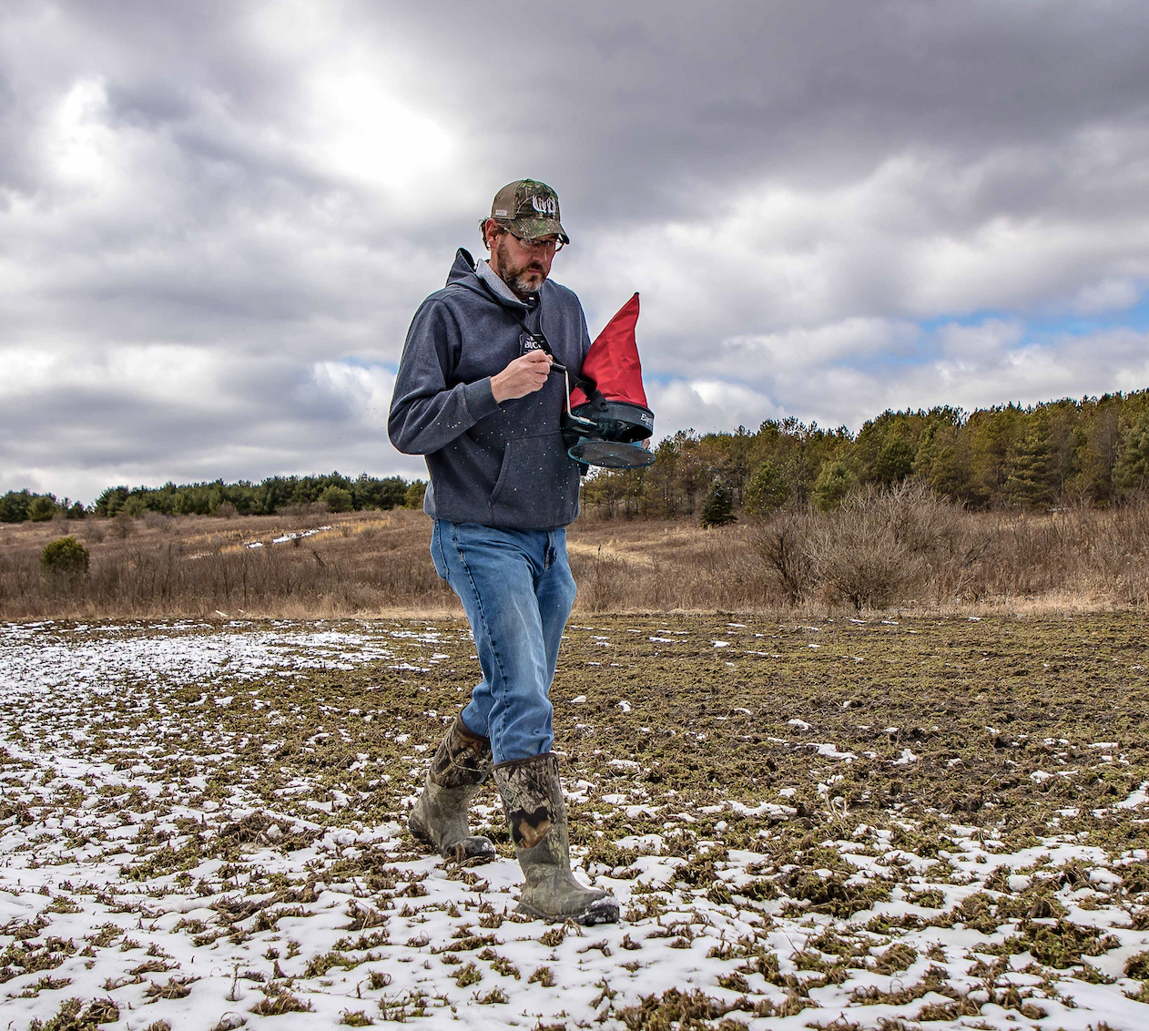 A man frost-seeds a clover field in early spring, showing when to plant deer food plots.