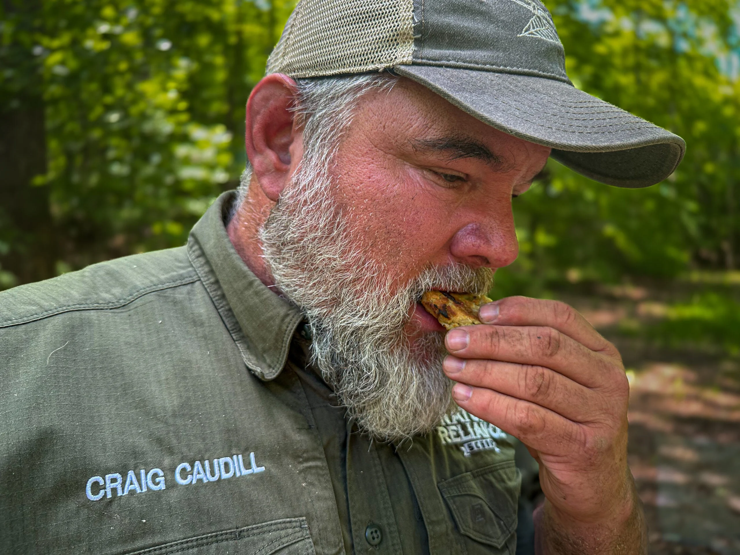 A man with a beard and a hat and green shirt eats a cookie