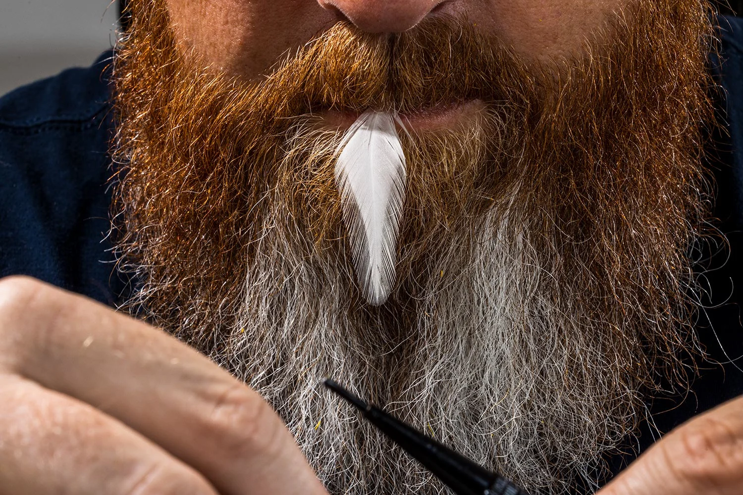 close-up of feather in Brandon Bailes's mouth as he ties a fly