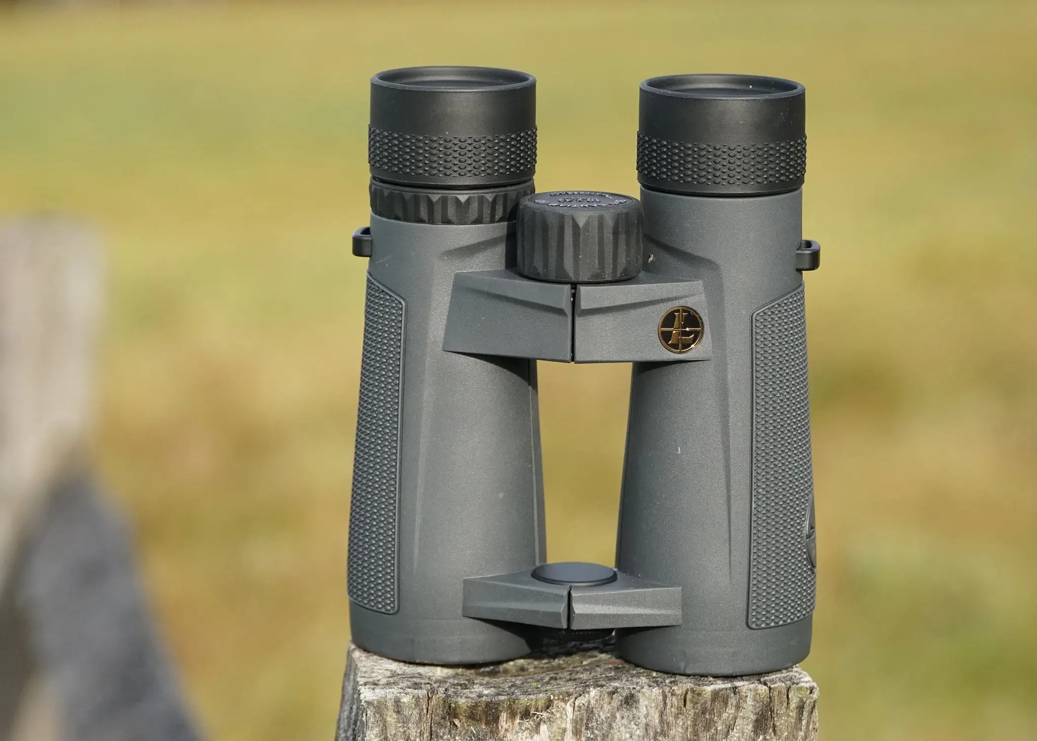 Leupold Santiam 10x42 binocular siiting on fence post with field in background.