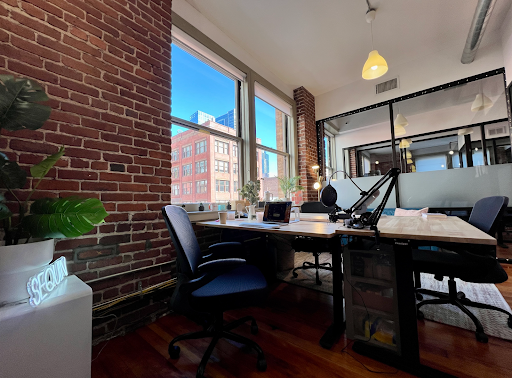 A room with exposed brick, a desk with a computer, and a window with a view of another building.