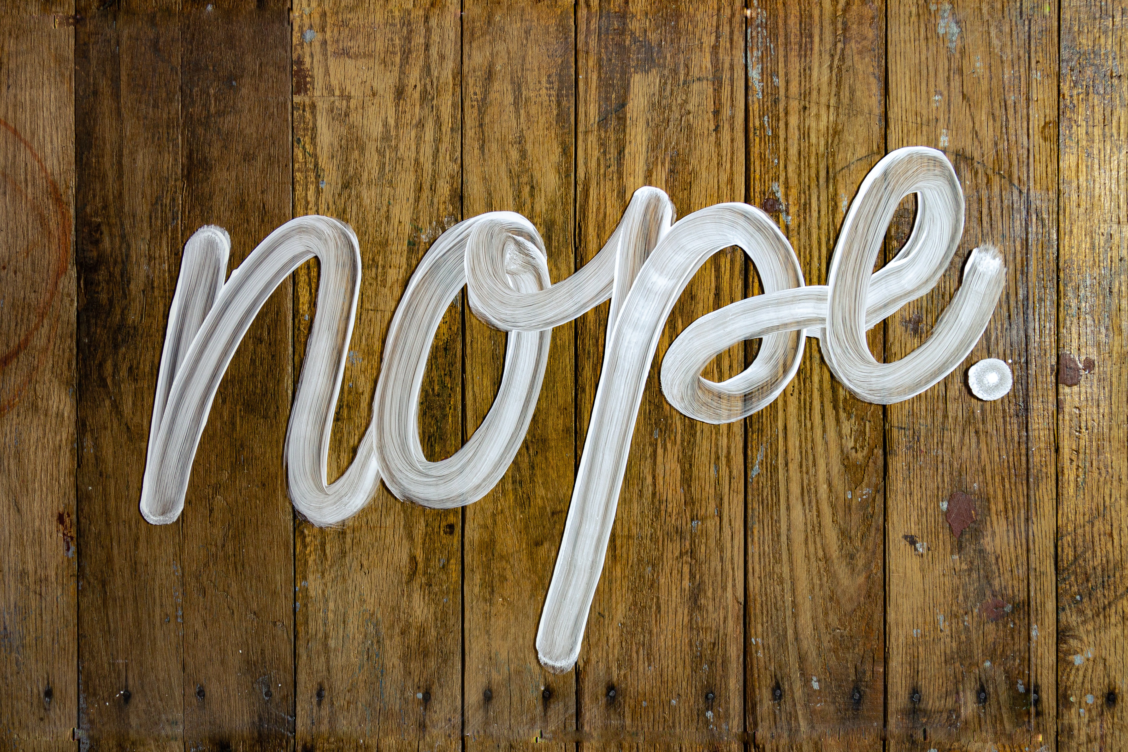 The word 'nope' written in cursive on a wood background