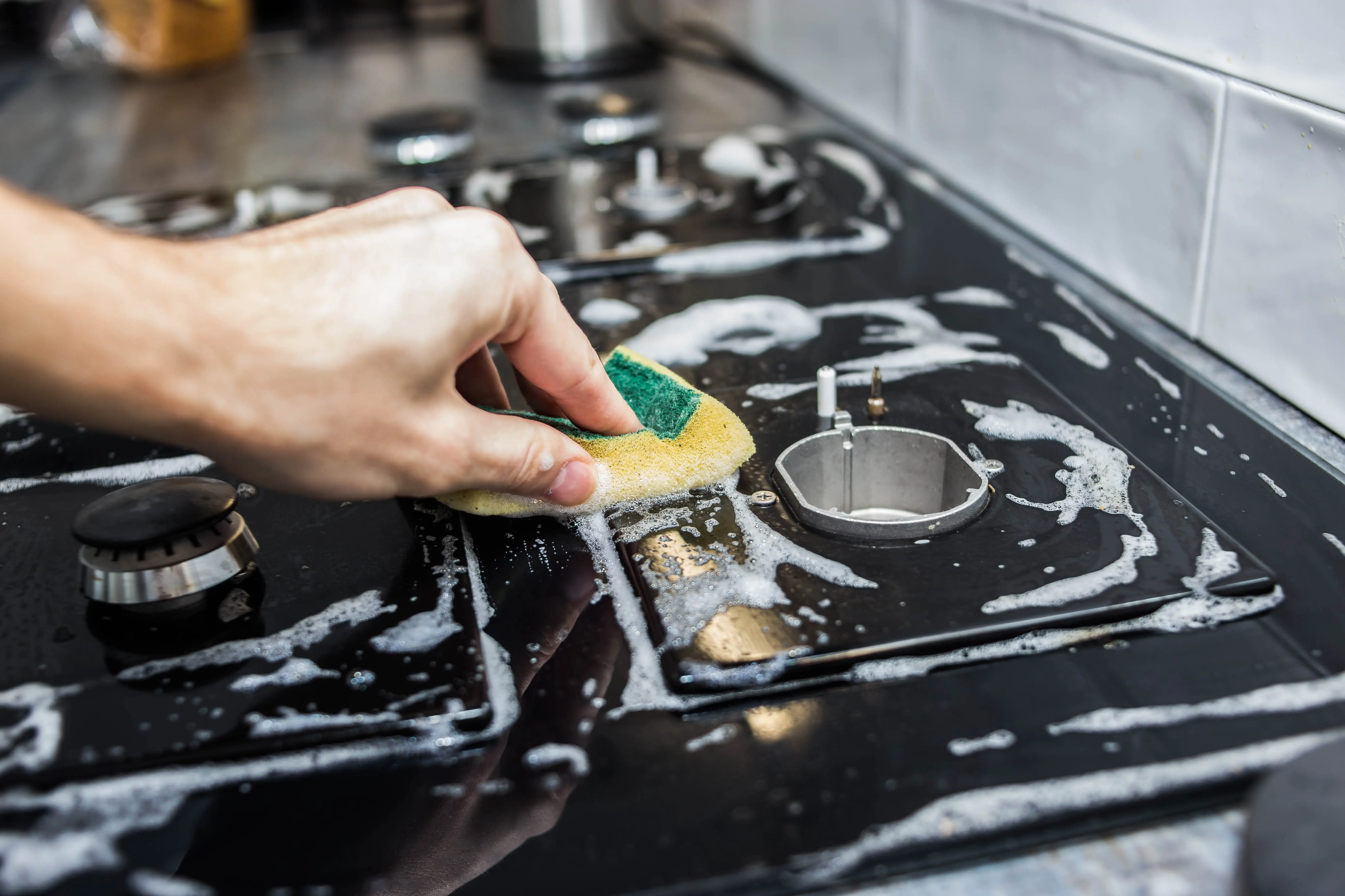 A person uses a sponge to clean a gas stovetop with soapy water