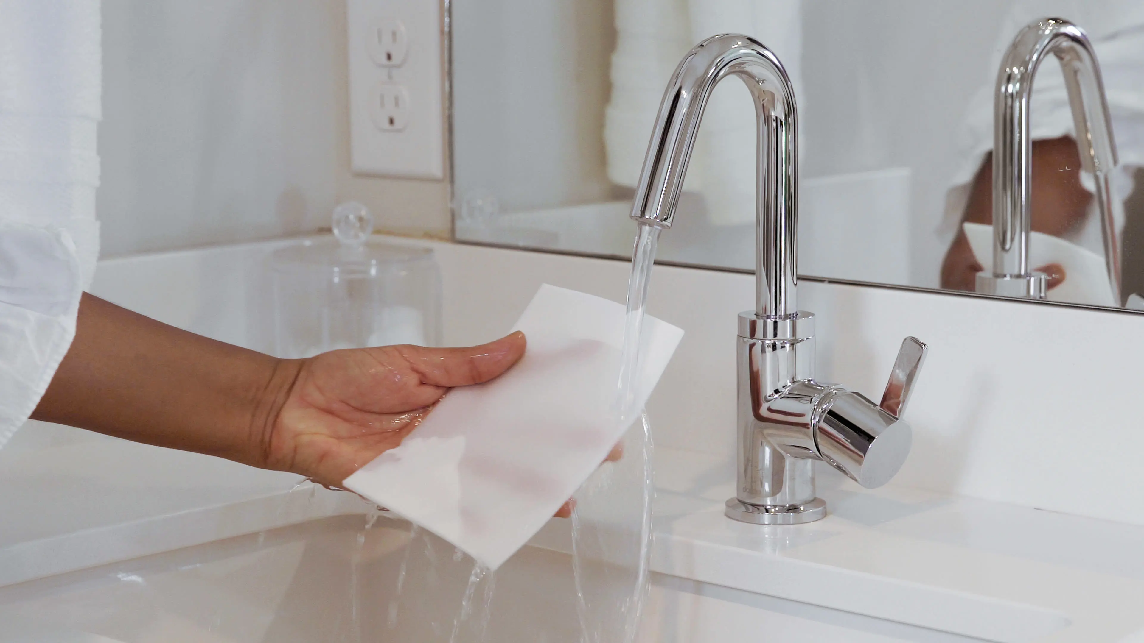 A person runs a Mr. Clean Sheet under a bathroom faucet