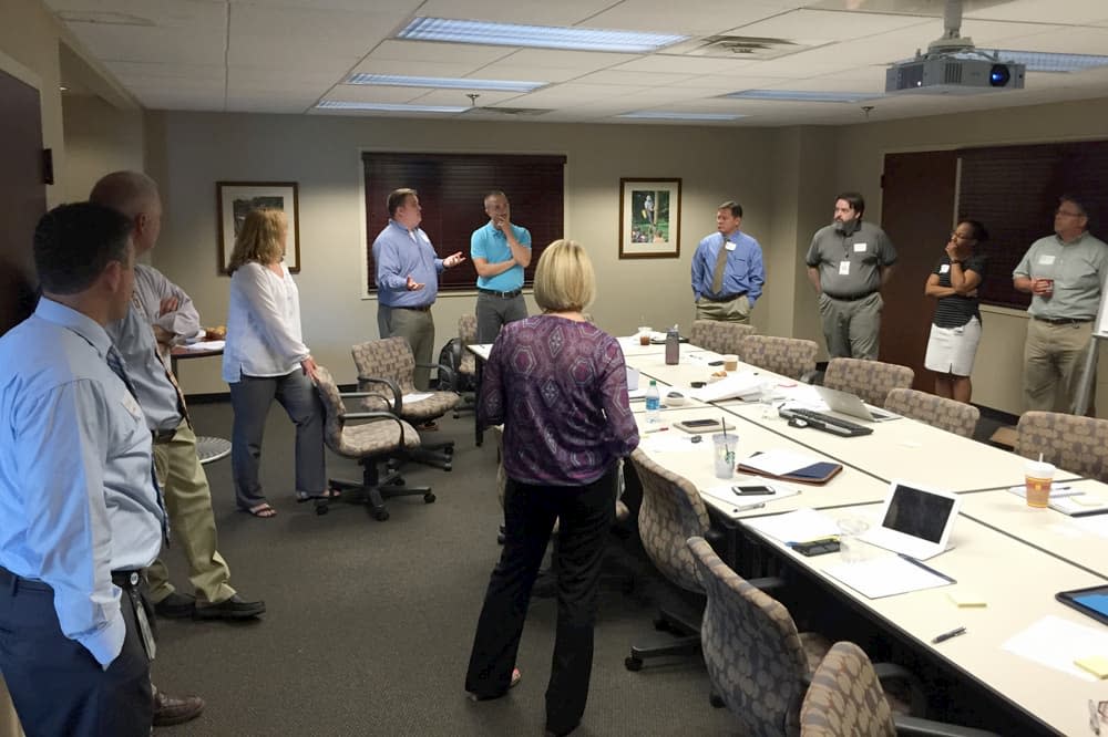 A team stands around a conference room in discussion during a Discovery