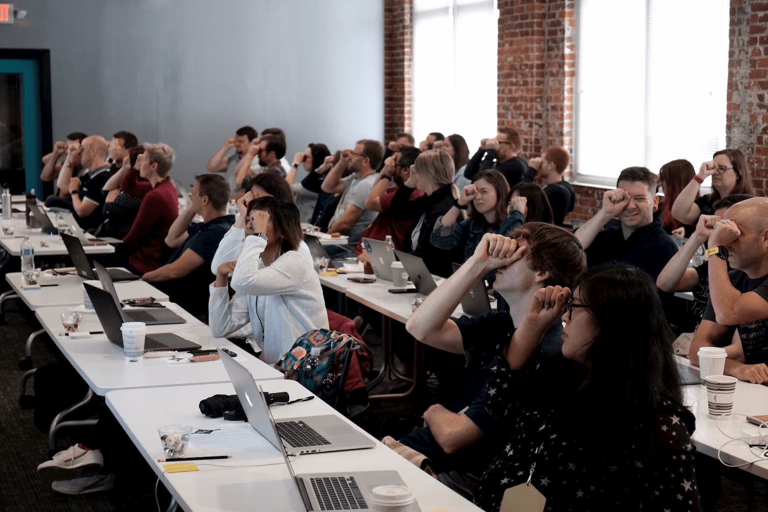 Audience members hold a fist up to one eye, looking through the opening in their fist at the screen in the front of the room.