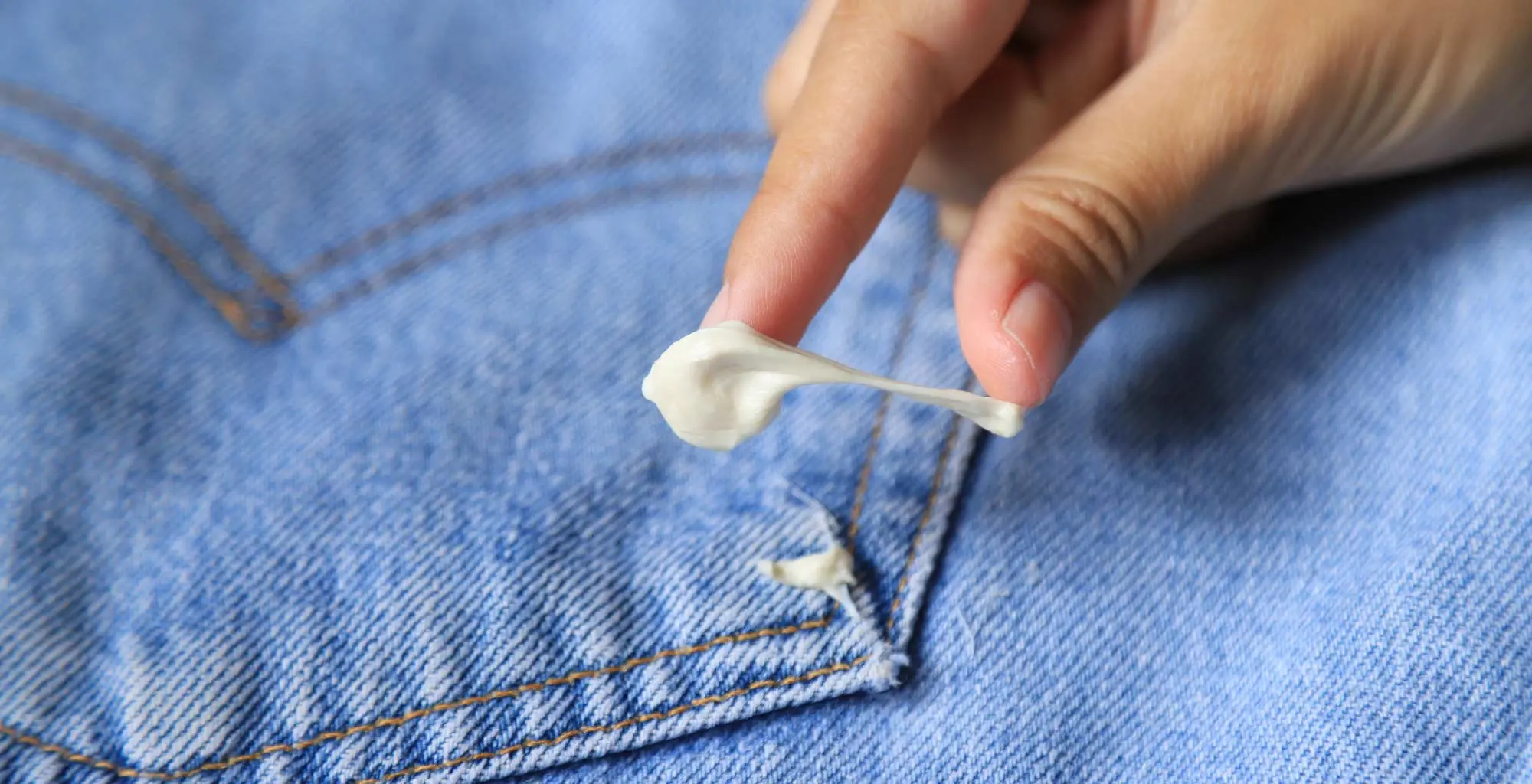Una mano intentando despegar un chicle del bolsillo de un jean.