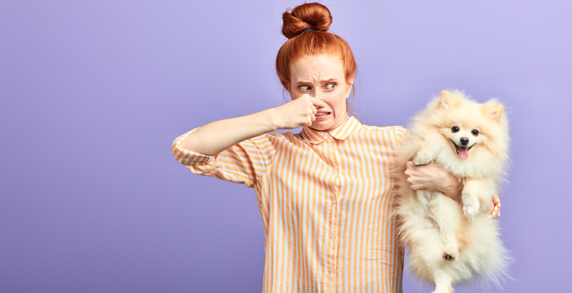 Una joven levantando su perro y tapa  ndose la nariz por su olor