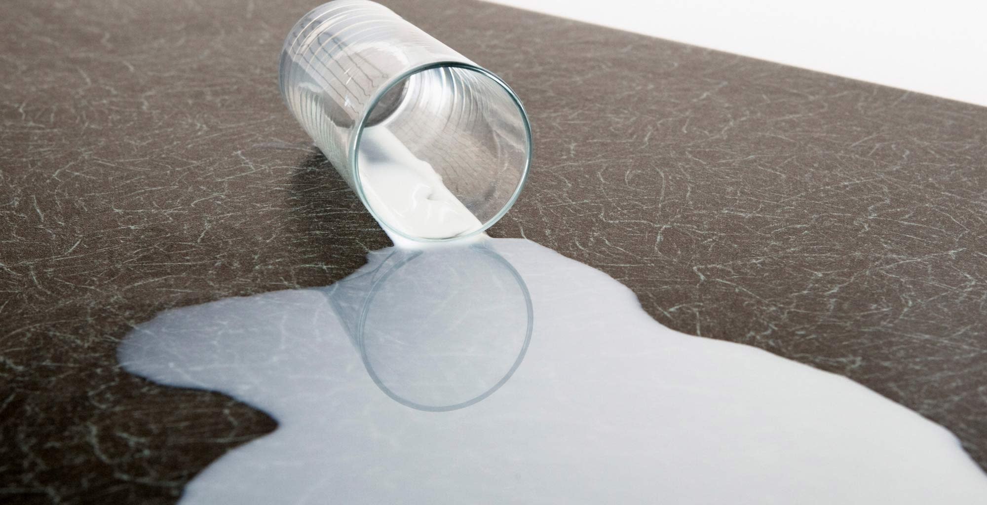 Un vaso de leche volcado sobre una mesa de mármol.